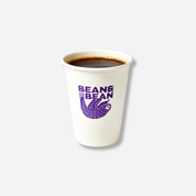 A small white paper cup filled with hot black coffee, printed with the “BEAN & BEAN” logo and a purple sloth illustration on the front.