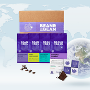 A Bean & Bean gift set featuring a branded shipping box, four purple bags of coffee with different labels, a coffee-and-chocolate pairing card, and assorted chocolate squares, shown on a light world map background with a small globe in the corner.