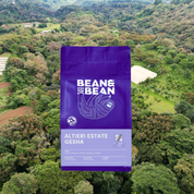 Purple Bean & Bean coffee bag labeled "Altieri Estate Gesha" set against an aerial view of a lush green farm.