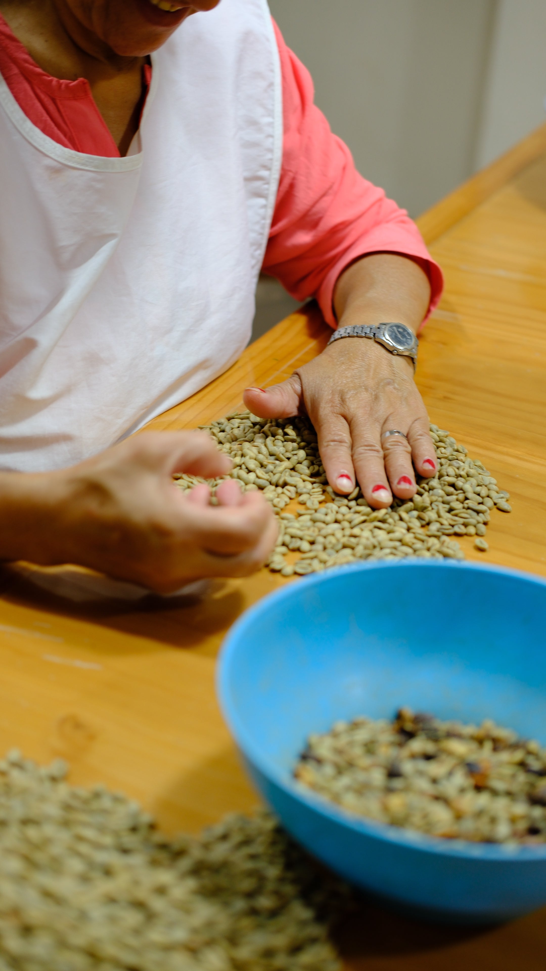 A woman hand-sorting unroasted green coffee beans on a wooden table.
