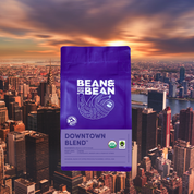 Purple Bean & Bean “Downtown Blend” coffee bag centered over a sunset skyline of New York City.