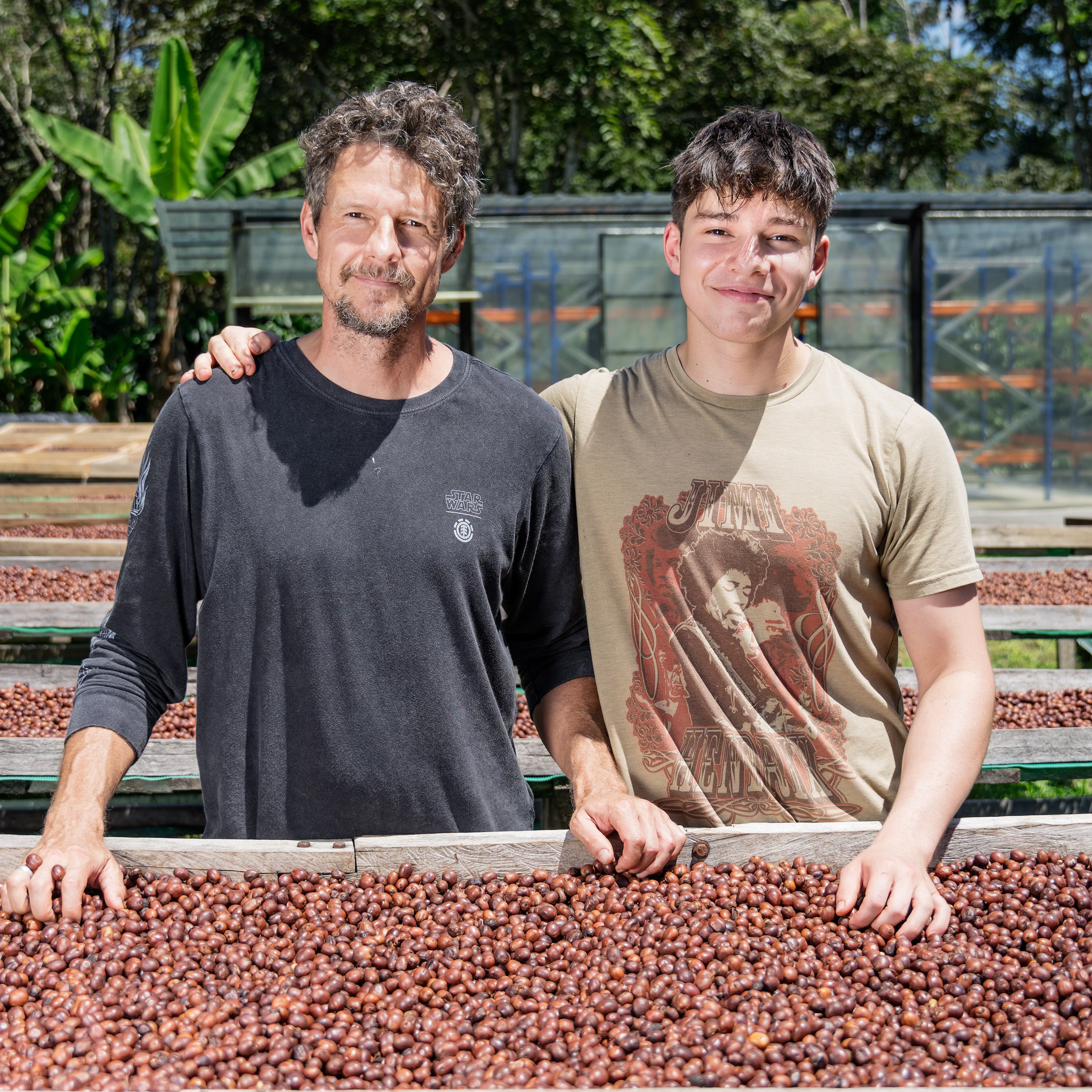 father and son standing in front of african bed of coffee cherries on a coffee farm