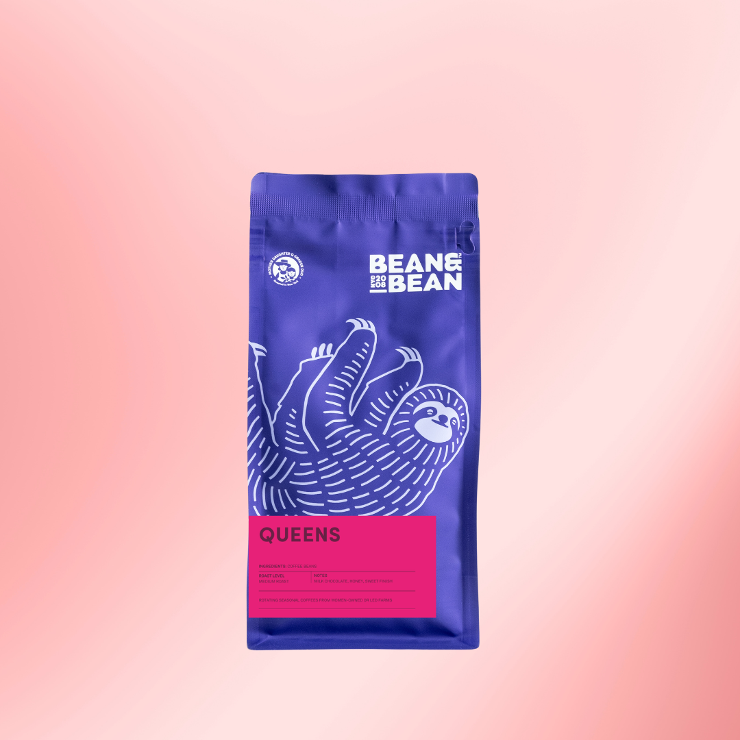 A purple Bean & Bean coffee bag with a large white sloth illustration and a bright pink “Queens” label, centered on a soft pink gradient background.