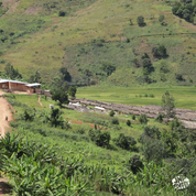 Coffee washing station in Burundi surrounded by lush green hills, with rows of raised drying beds and small buildings in the distance.