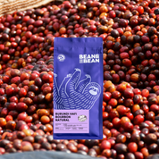 A Bean & Bean bag of Burundi Hafi Bourbon Natural coffee against a background of red coffee cherries.