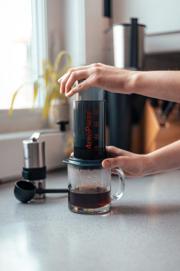 Pair of hands using Aeropress Coffee Maker on a kitchen counter