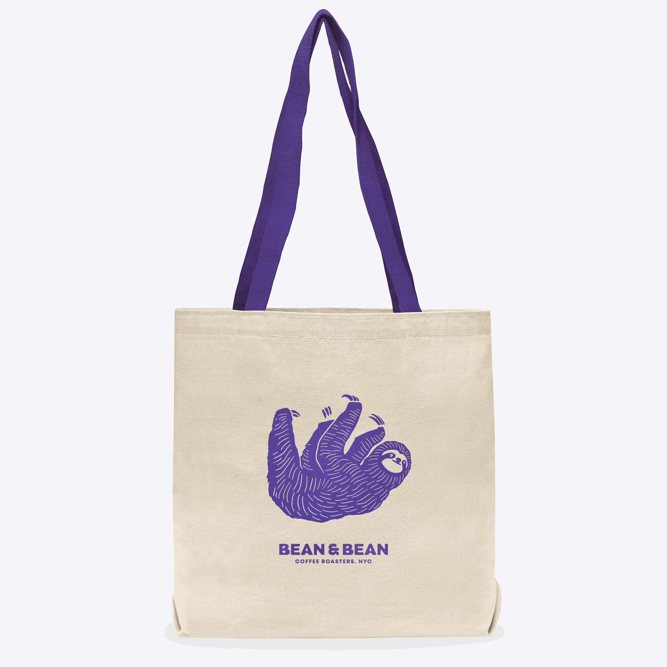 Beige tote bag with purple handles, featuring a purple illustration of a smiling sloth and the text 'BEAN & BEAN Coffee Roasters, NYC' on the front.